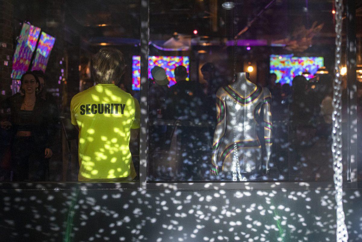 A man in a neon shirt stands with his arms crossed next to a mannequin.