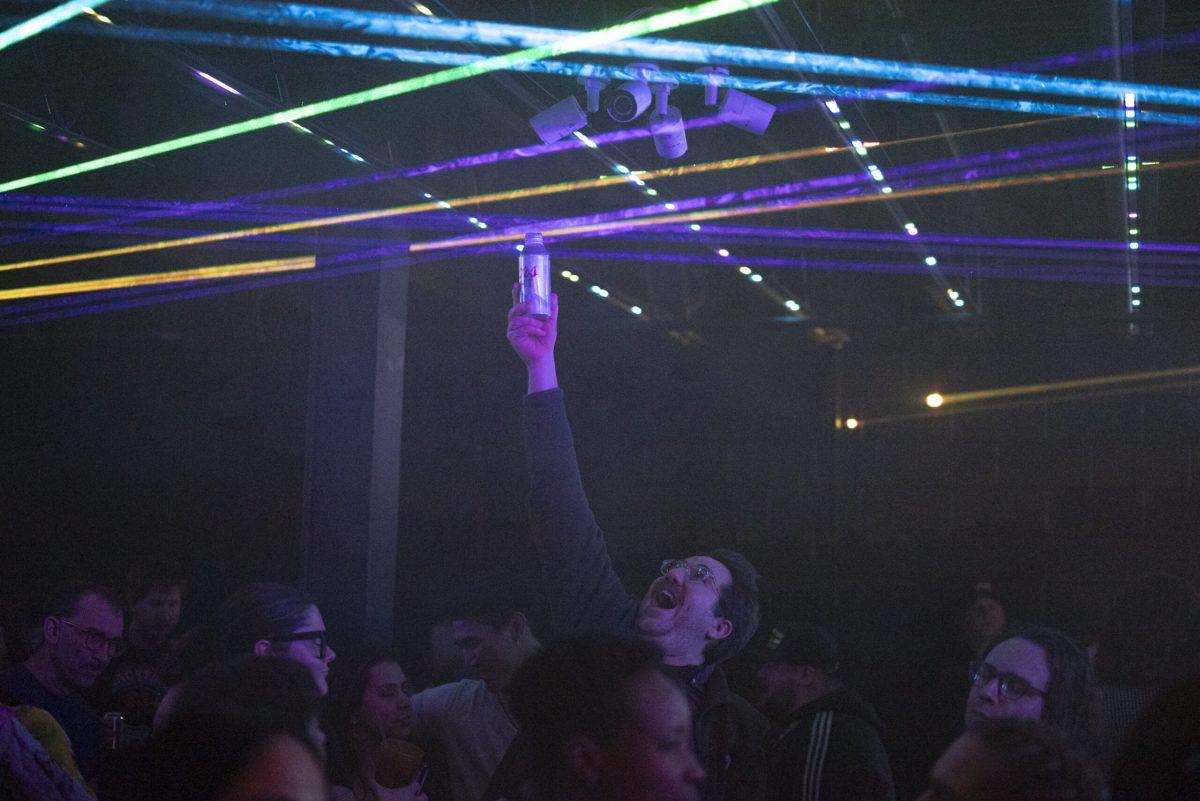 A man reaches above his head with a beer can.