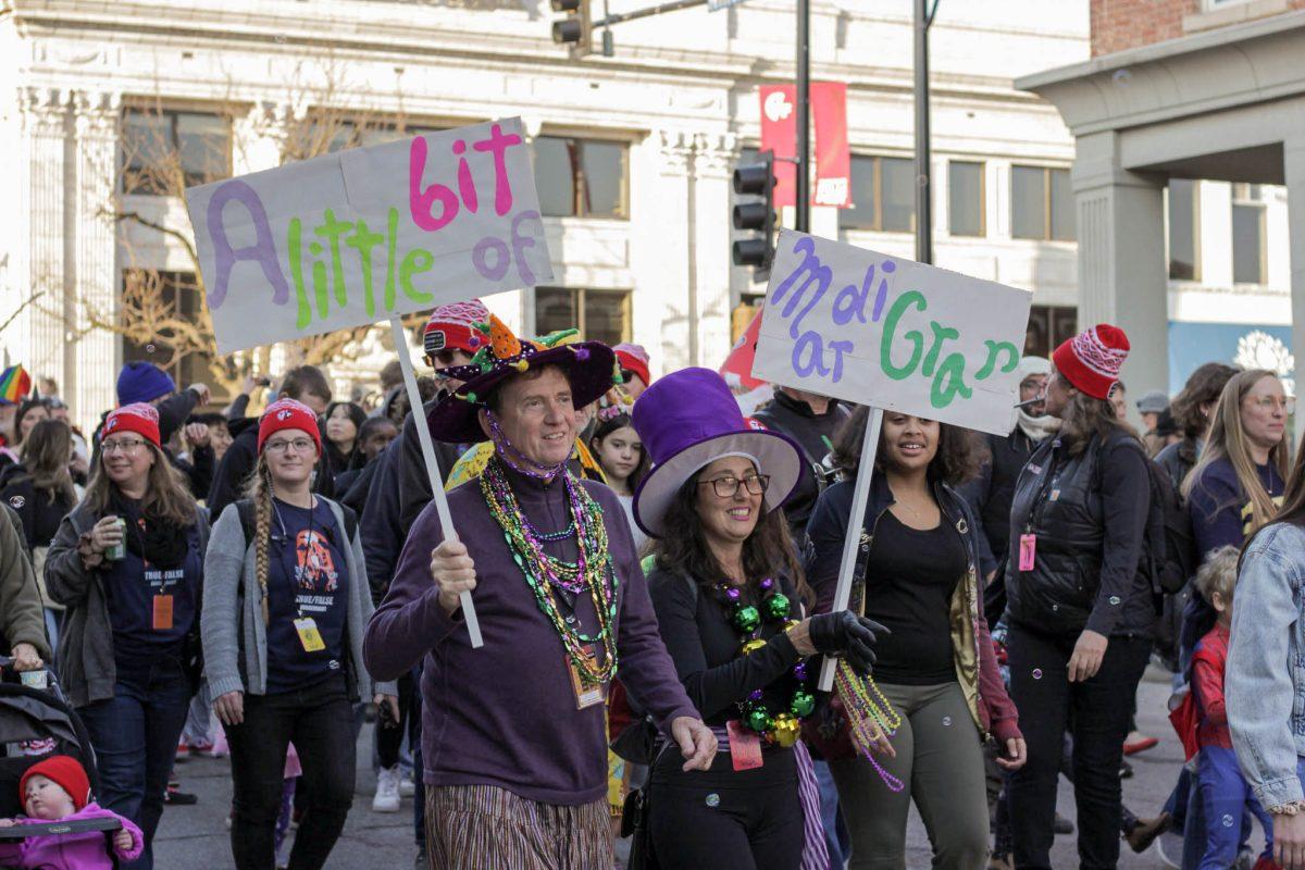 A couple holds signs saying, “A little bit of Mardi Gras,” while walking in the parade.
