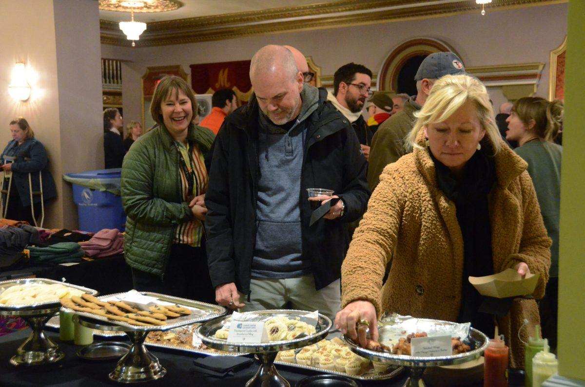 A man and a woman look at a buffet while grabbing food.
