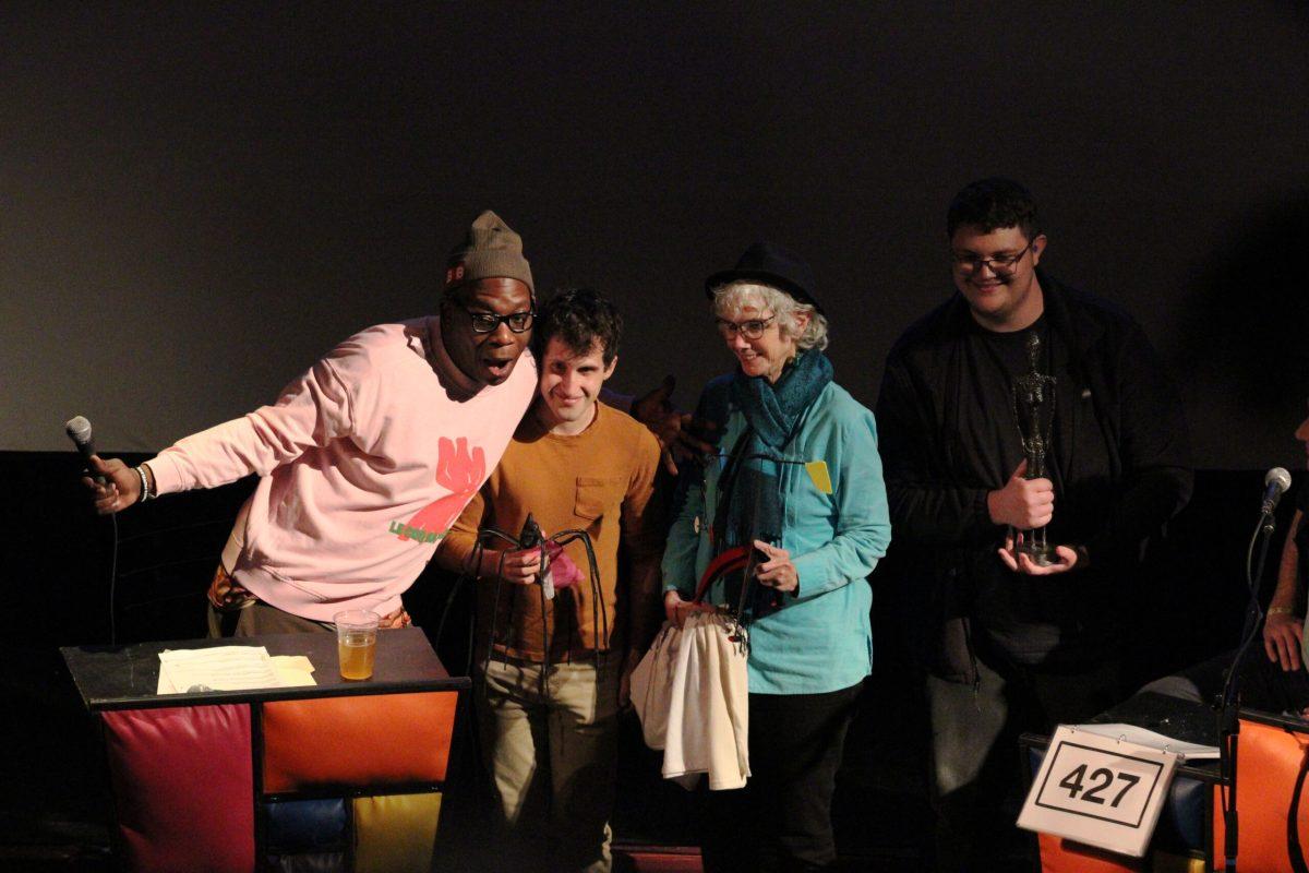A man poses on stage with two men and a woman.
