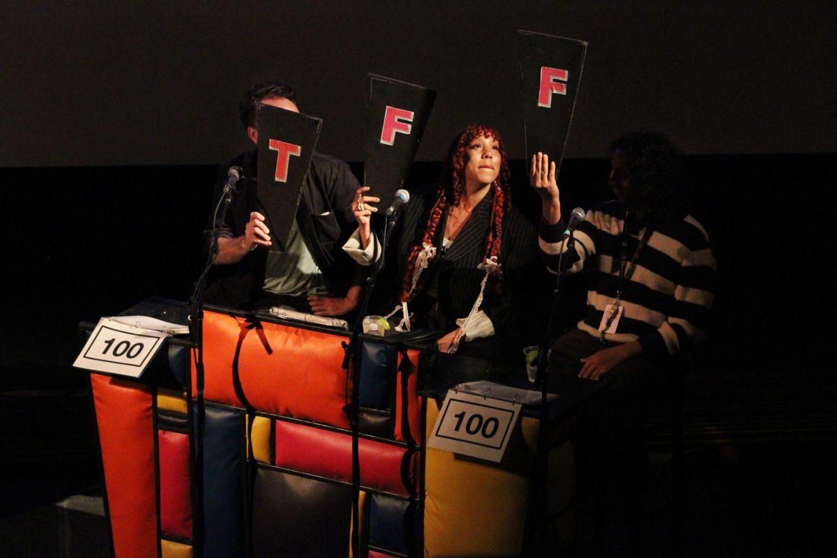 A woman holds up a sign with an “F” on it while another man holds up a “T” to the left and another man holds another “F” to the right.