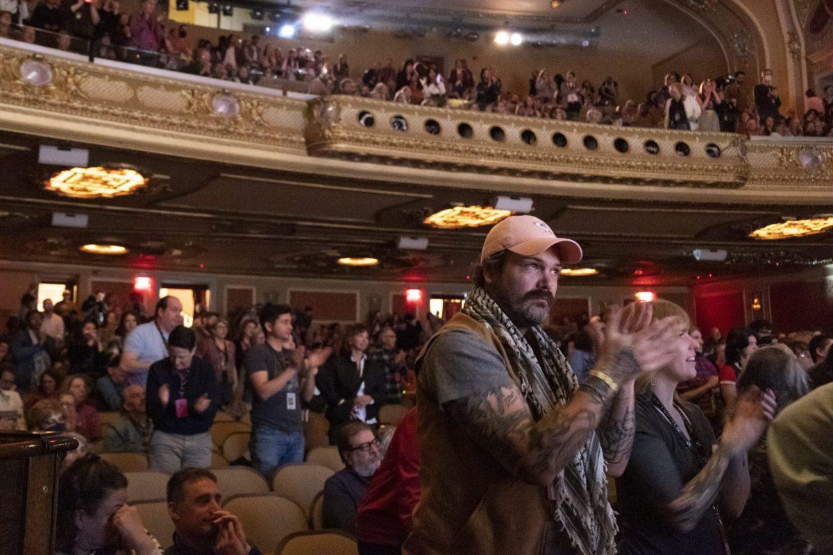 A man stands and claps as the crowd claps in a theater.
