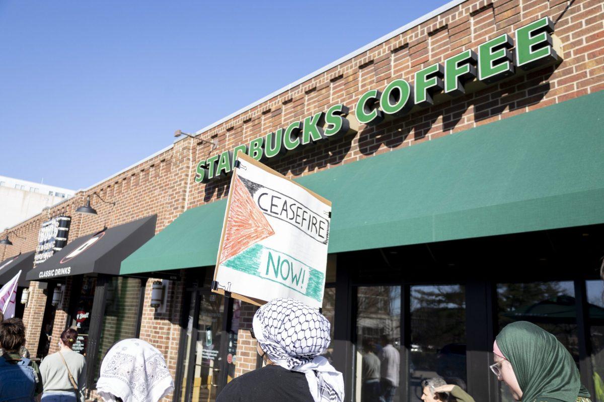 A protester holds up a “Ceasefire Now” sign in front of a Starbucks.
