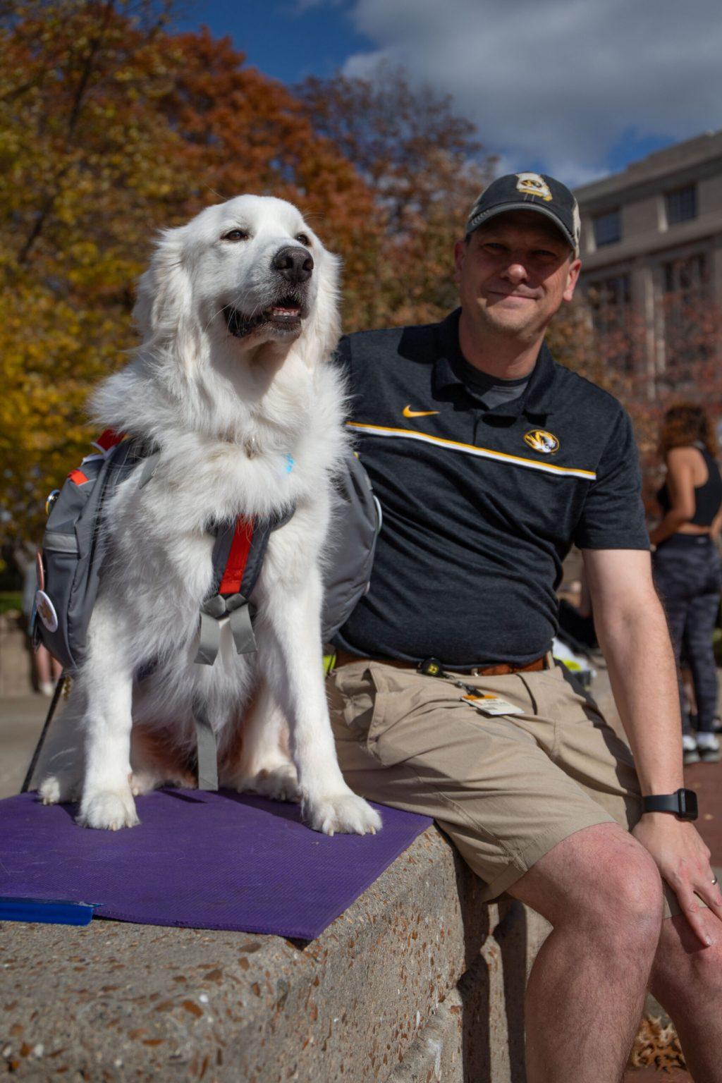 Jason Furrer, right, sits next to Luna, left, on a rock wall and smiles at the camera.