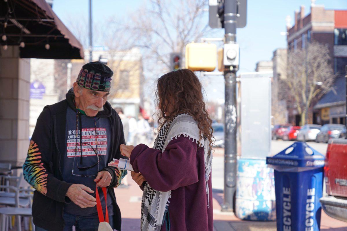 A man hands a woman a stack of fliers.