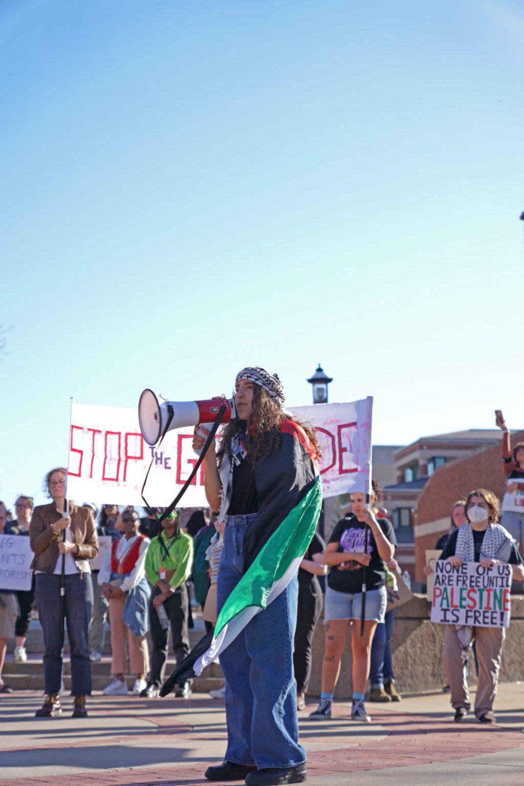 A woman stands in front of a crowd, speaking into a megaphone.