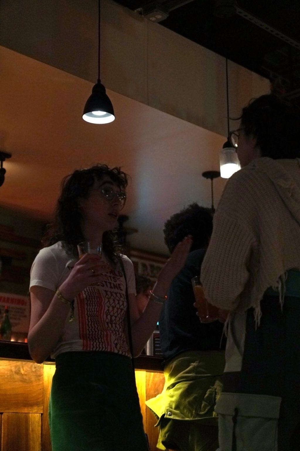 A woman talks to her friend while holding a drink.