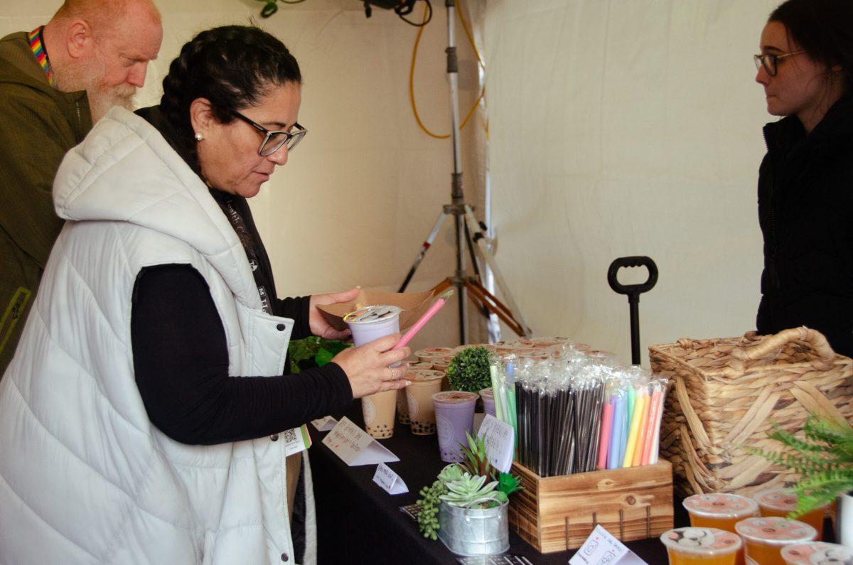 A woman holds a purple drink and a straw while standing in front of a table.

