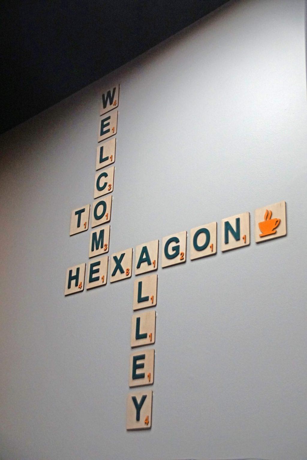 Against the doorway, a sign reads “Welcome to Hexagon Alley” with scrabble letters.
