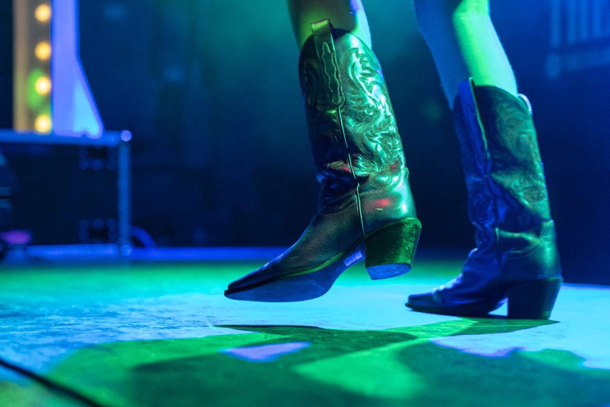 Cowboy boots are worn on a stage with the left boot raised.