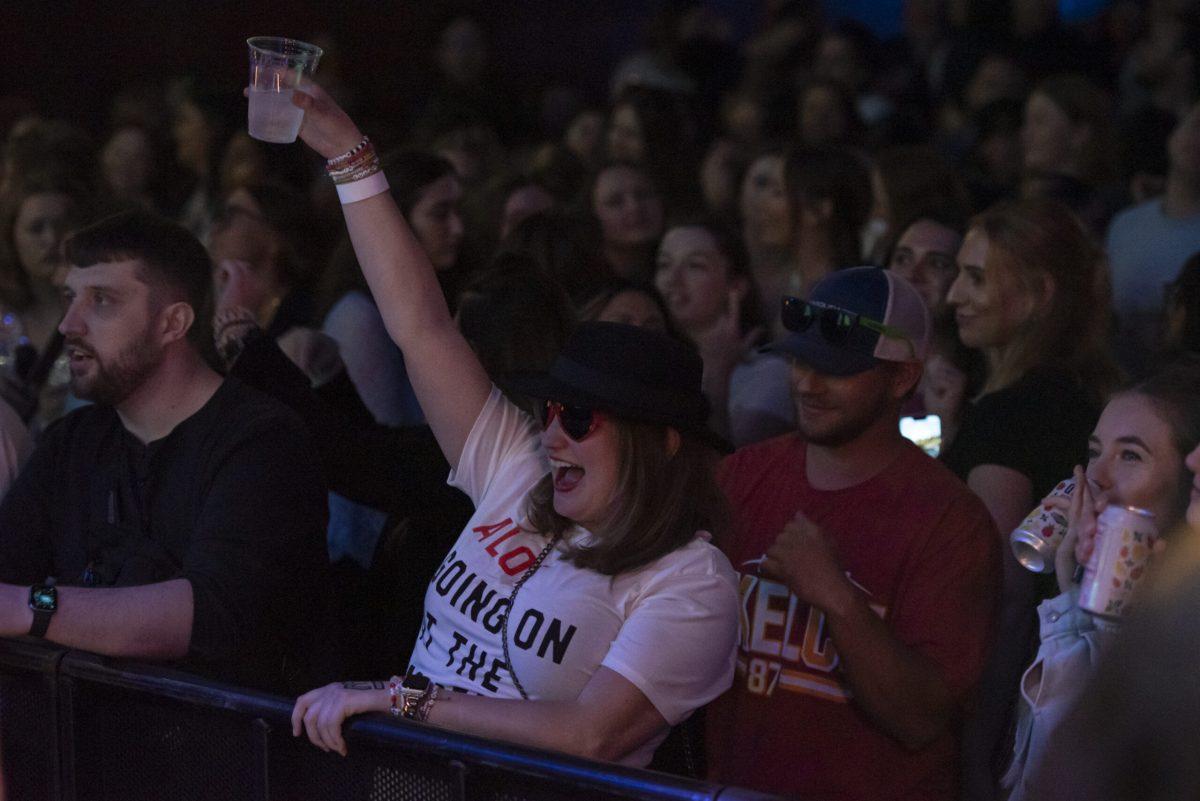 A woman stands in a crowd with a drink raised above her head.