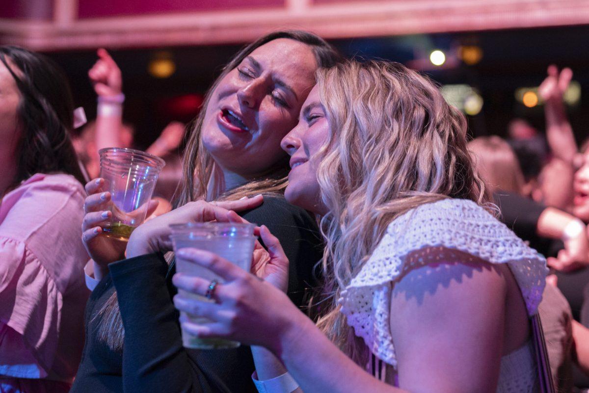 Two women sing together while holding drinks.