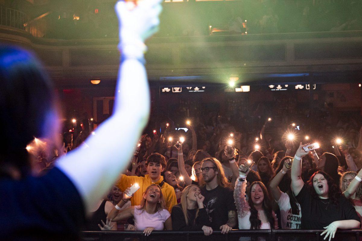 A woman on stage holds an iPhone above her head facing a crowd doing the same.