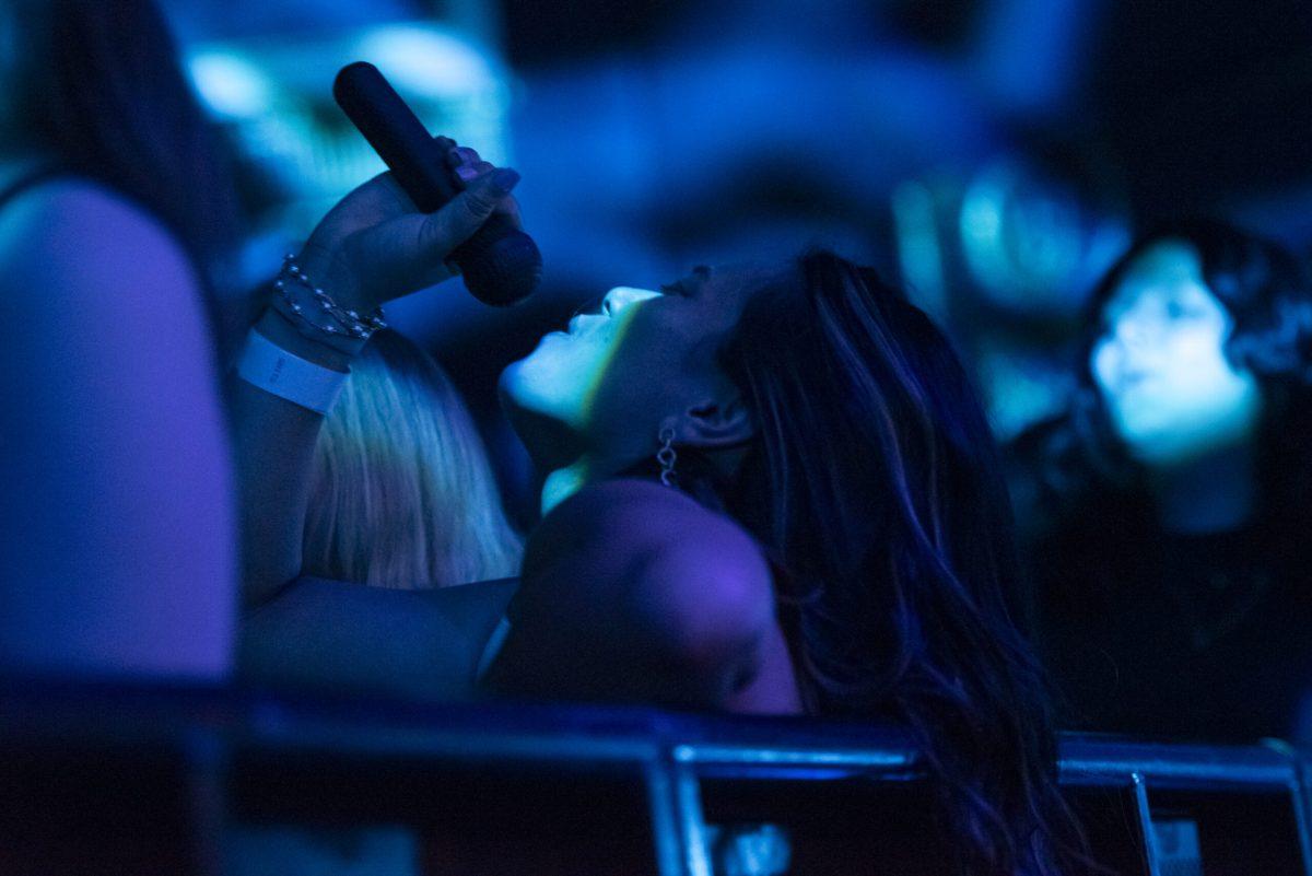 A woman holds a microphone above her mouth while leaning against a barricade.