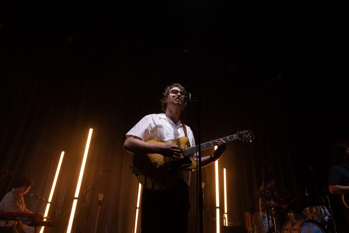 A man sings into a mic and strums a guitar on a stage.