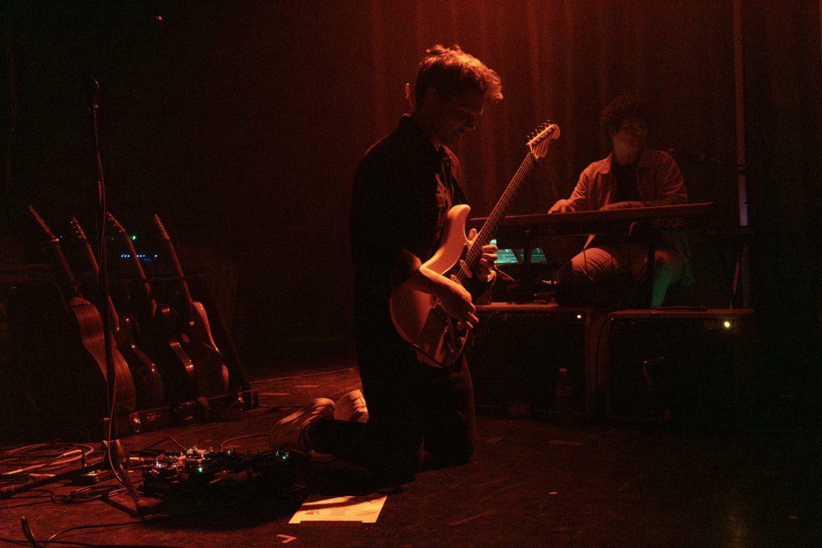 A man kneels while playing his guitar on stage.
