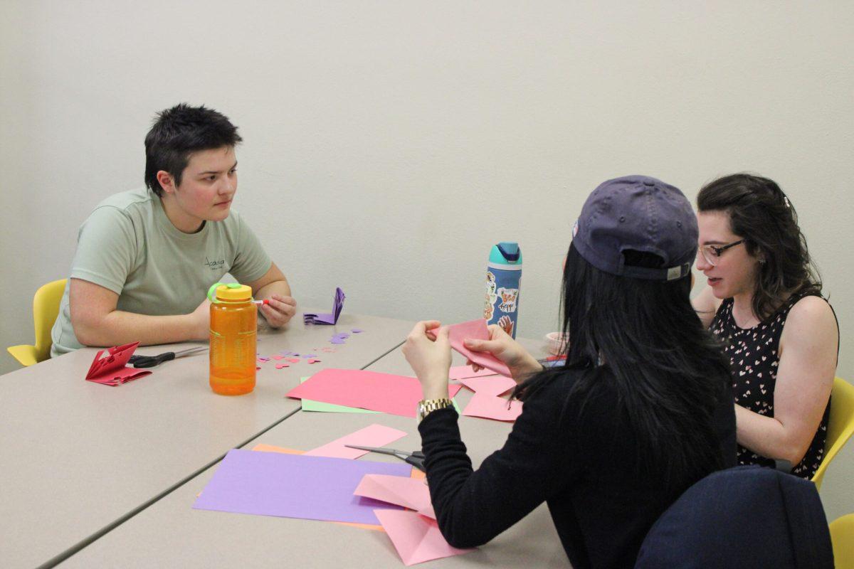 Students sitting at a table engaged in conversation while folding paper.