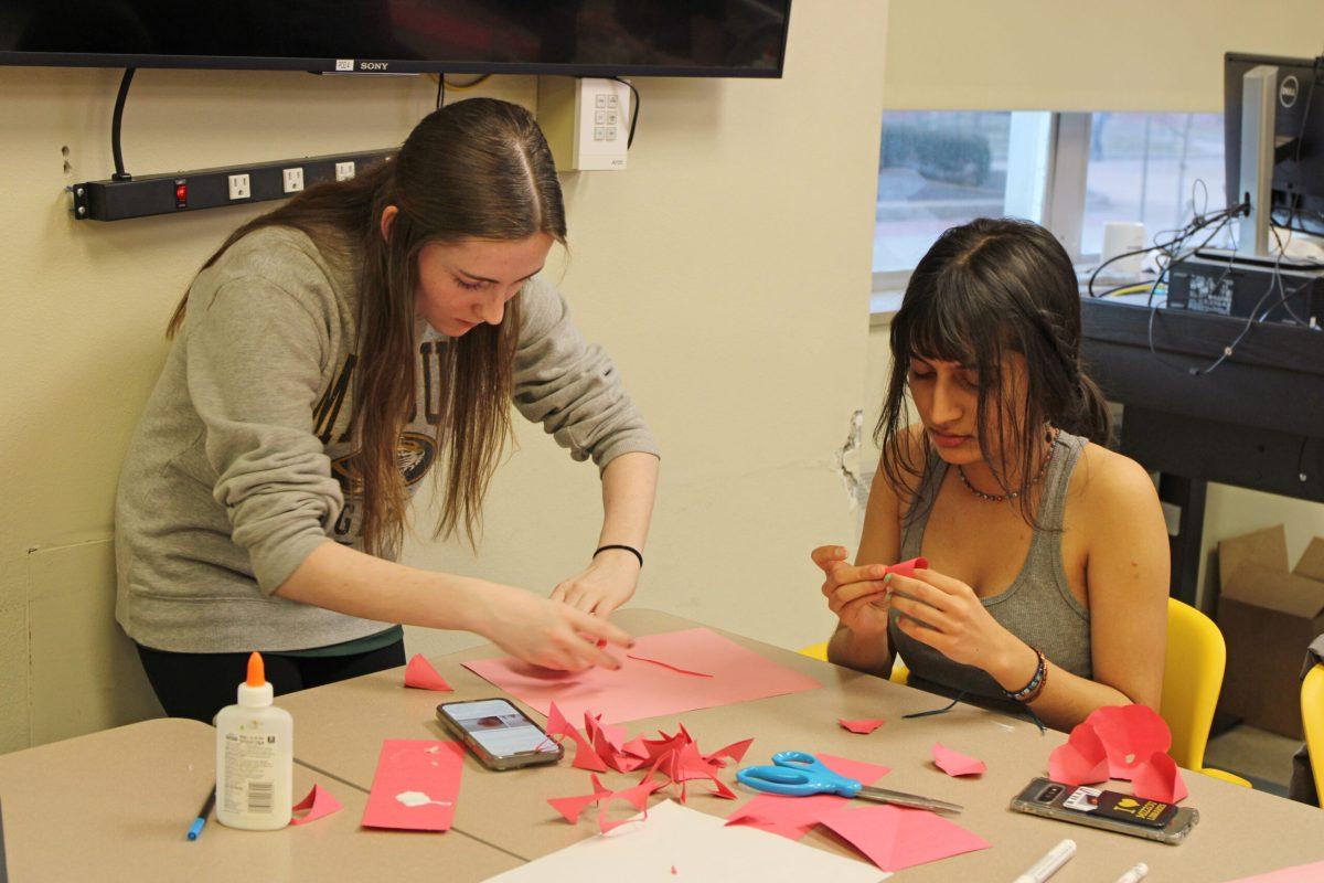 Two girls fold sheets of red and pink paper.