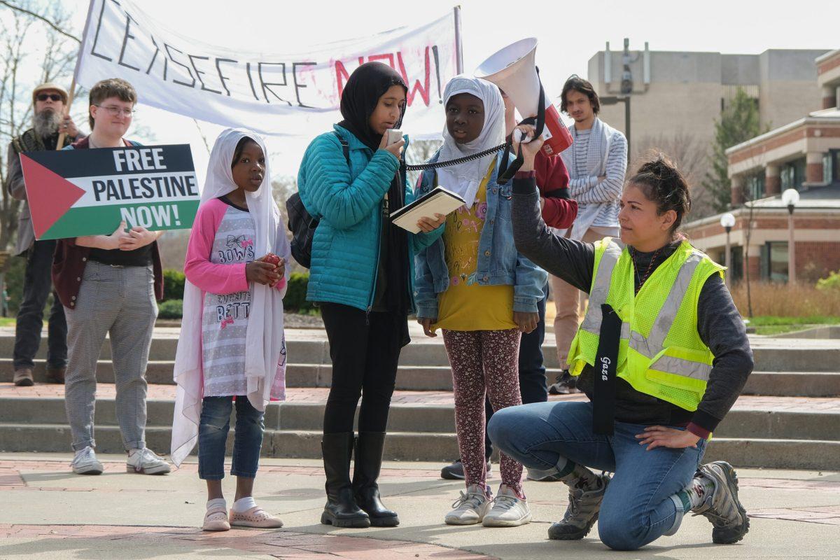 Three little girls read the notebook in the speech circle and there is a woman holding a megaphone for them.