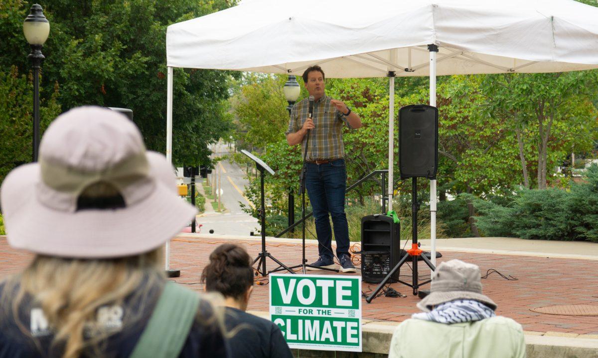 A man speaking on stage in front of a Vote for the Climate sign.