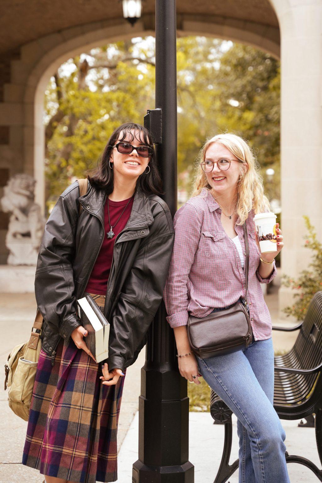 Two girls leaning against a lamppost.