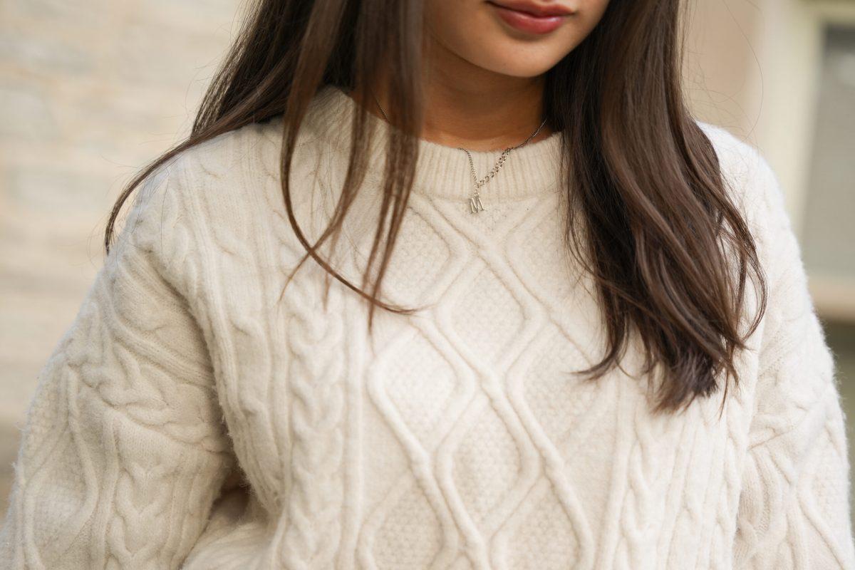 A girl standing wearing a cream-colored sweater.