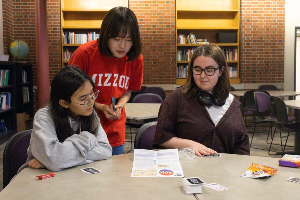 Three students looking at instructions for how to play Fluxx.