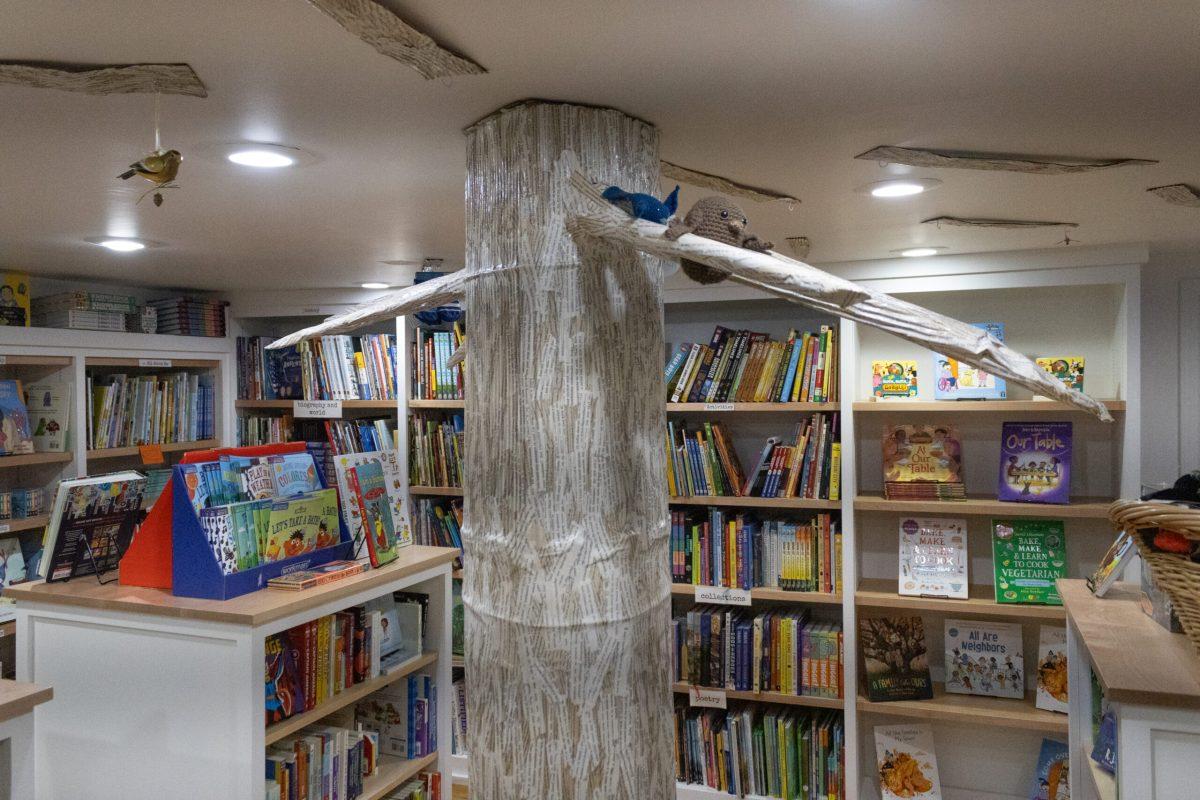 A large paper mache tree holding crocheted birds sitting in the middle of a room filled with books.