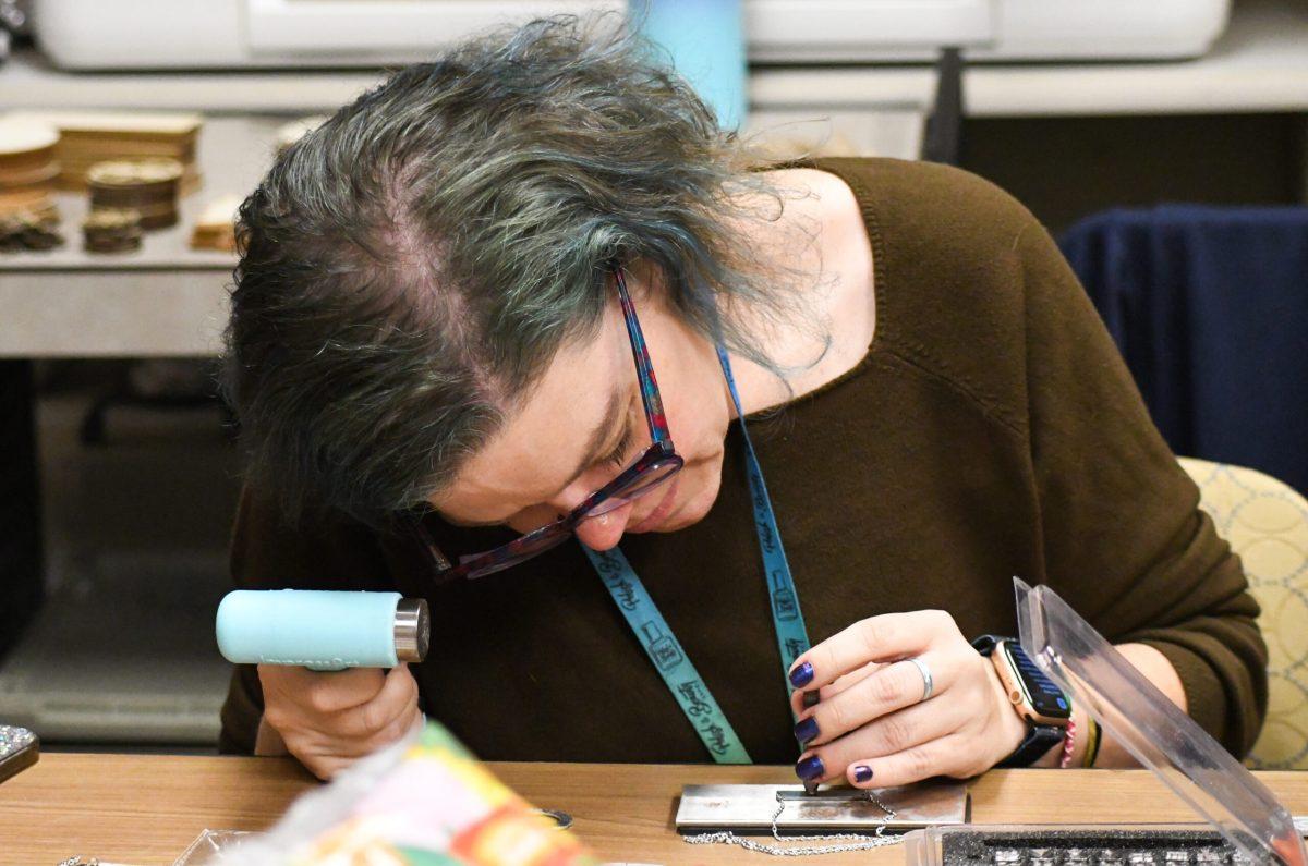 A woman hammering letters into a metal necklace.