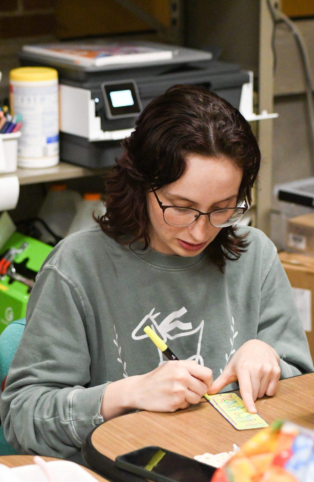 A student using markers to color wooden bookmarks.