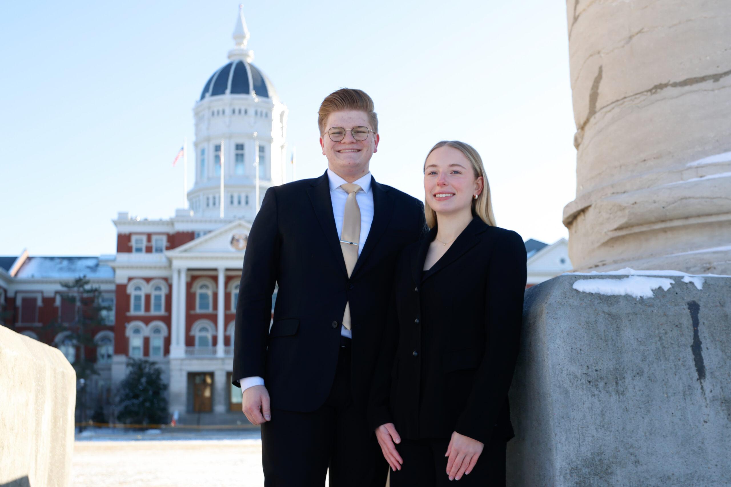 A man and a woman stand together in front of the Columns.