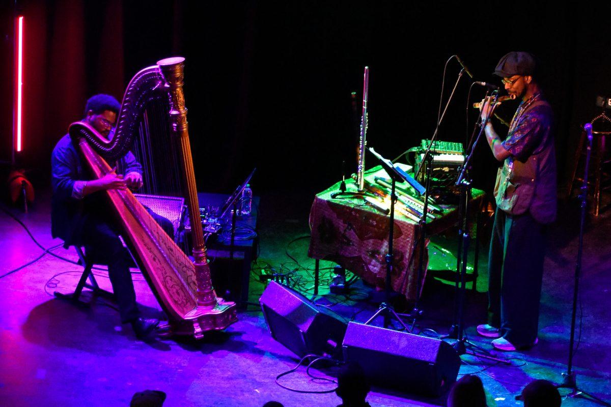 A man plays a flute while another man plays a harp.