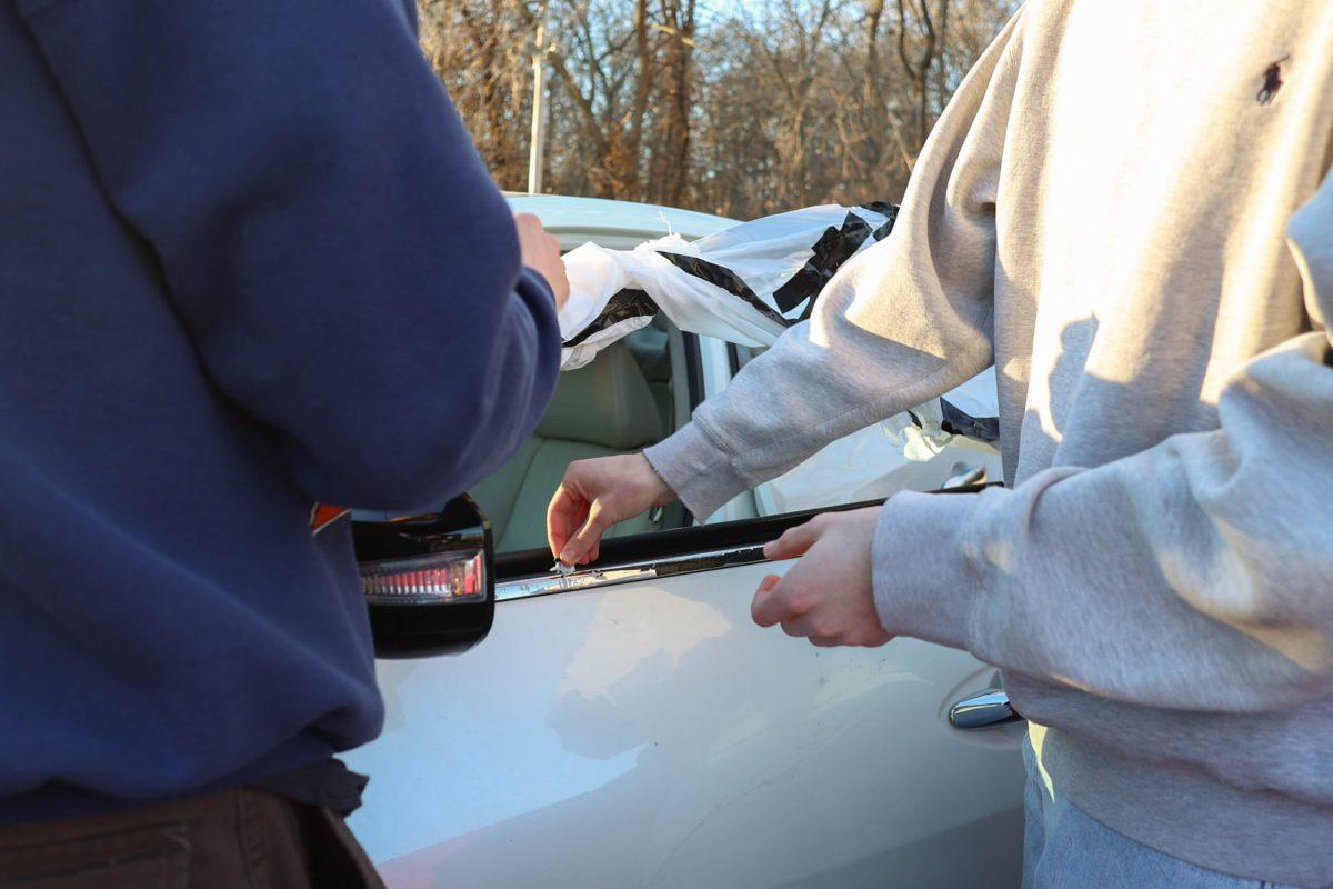 Two people taping up a car window.