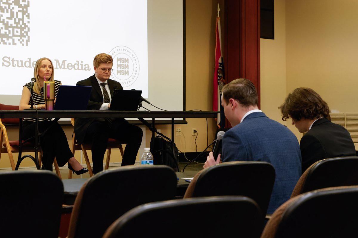 Two people listen as a moderator asks a question.