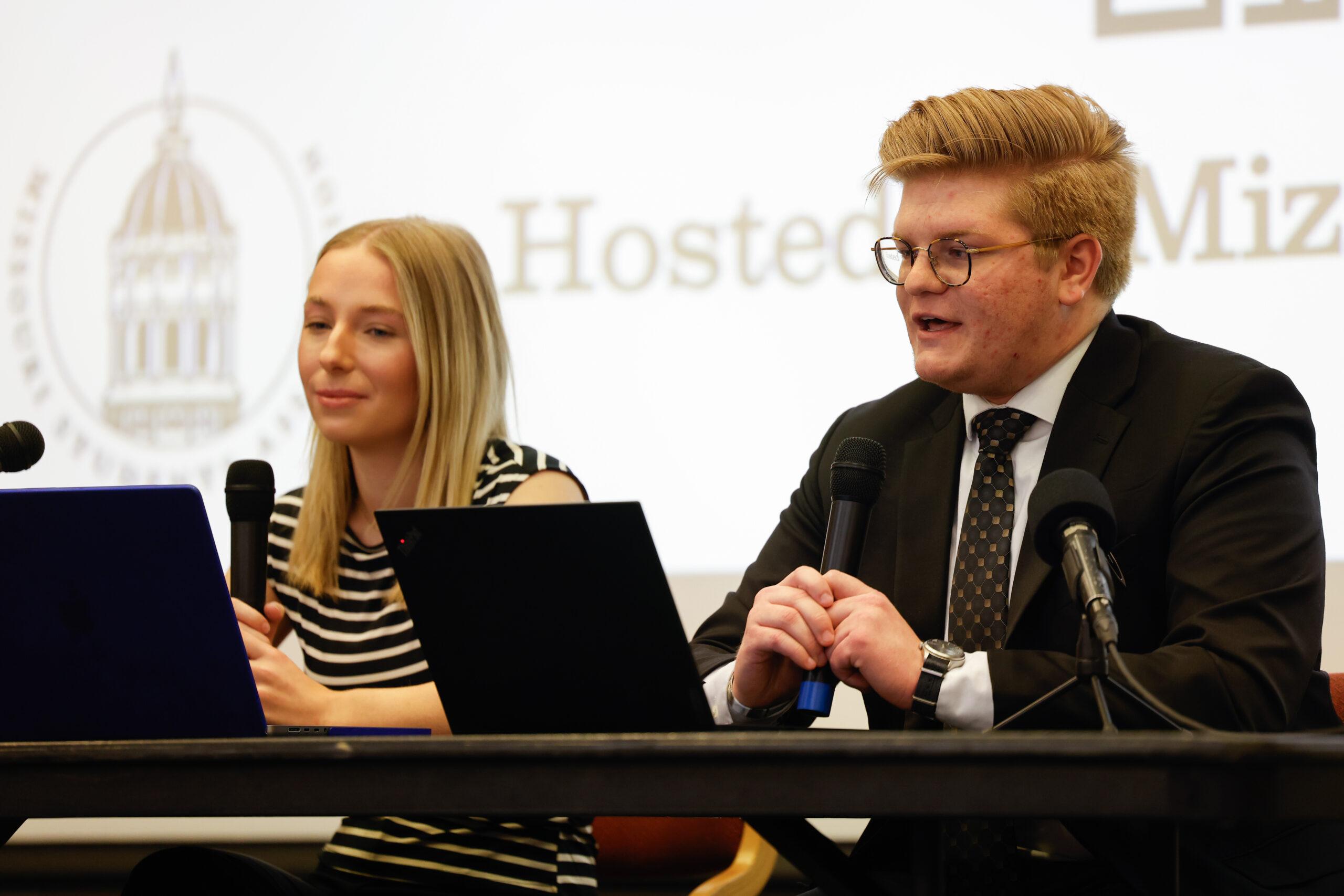 A man speaks into a microphone next to a woman.