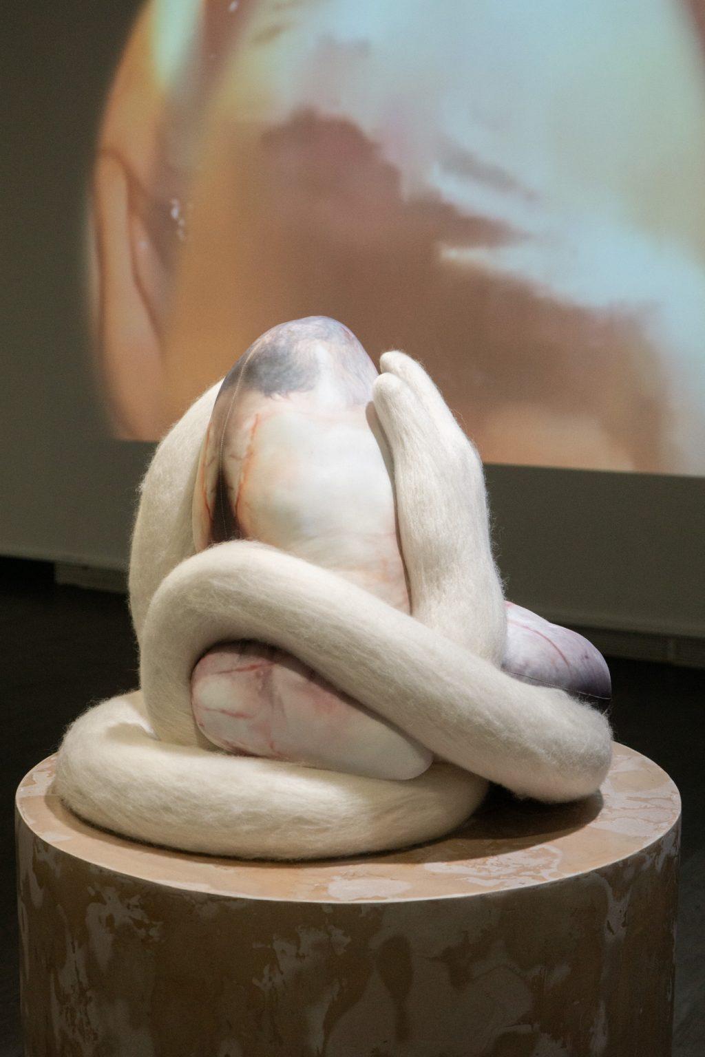 An art piece sits on a pedestal in front of a projection.