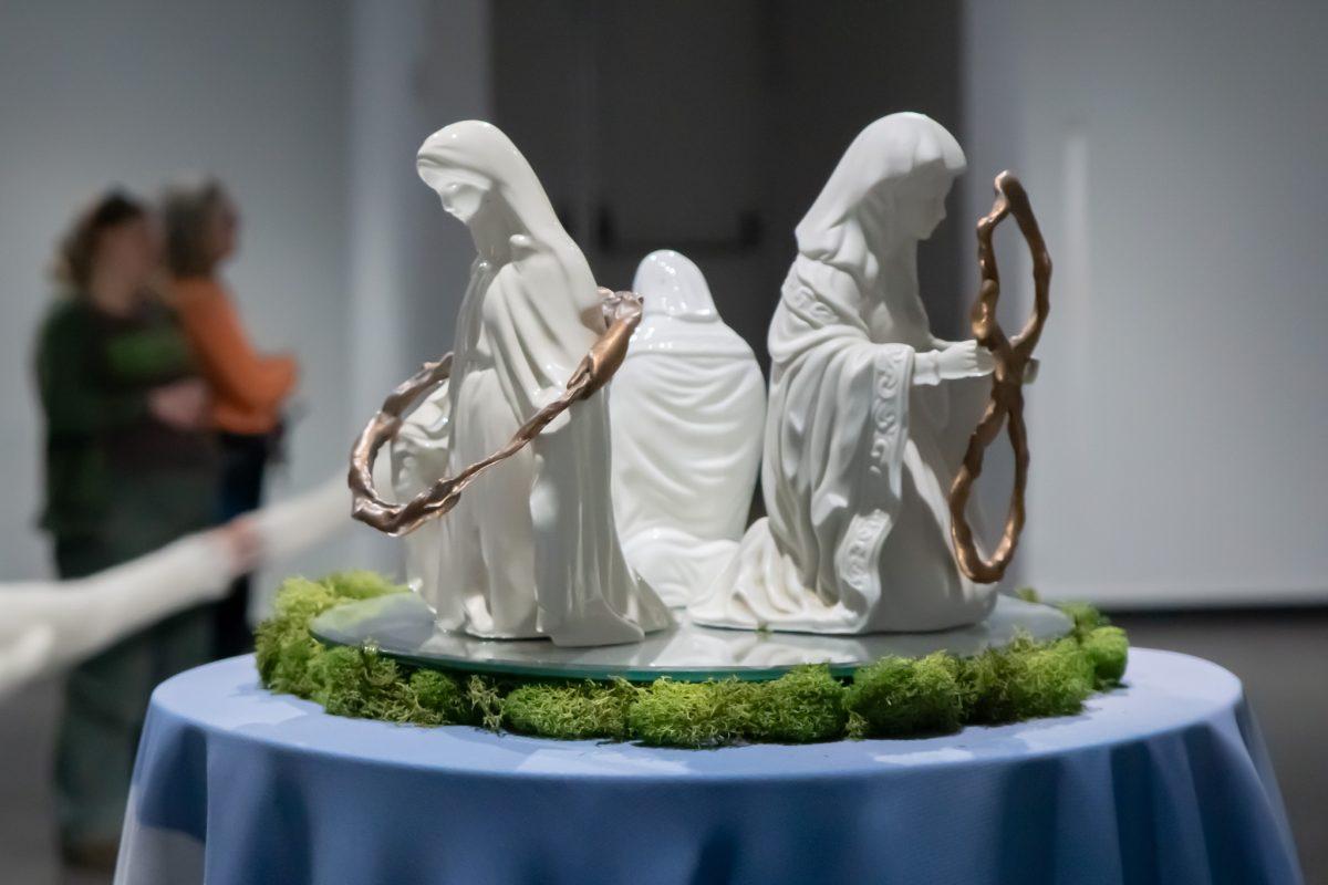 Figures sit on display as visitors view the work.