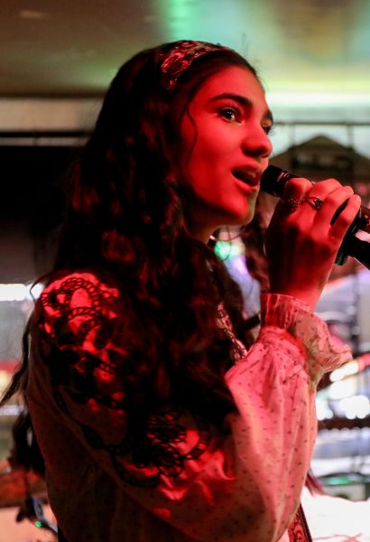 A woman sings under a red spotlight.