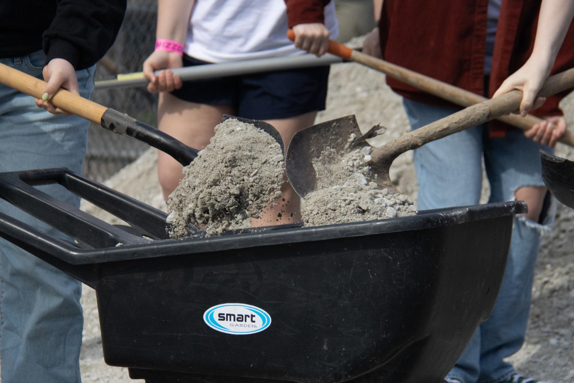 People dumping gravel into a wheelbarrow.
