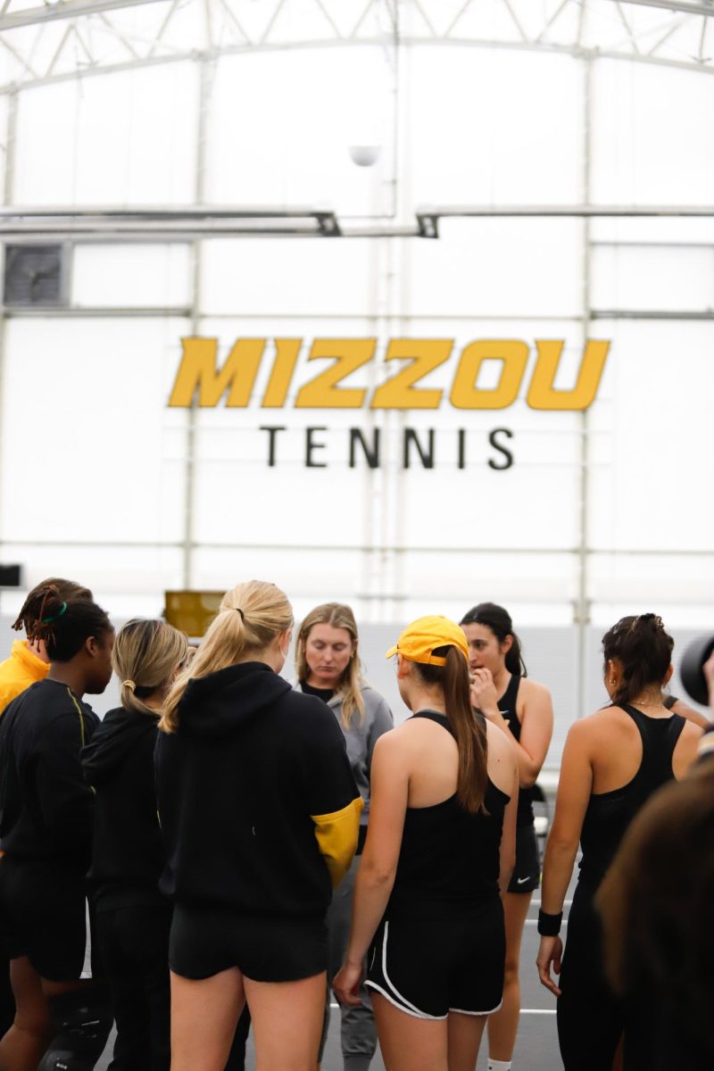 Tennis players stand together under the Mizzou Tennis logo.