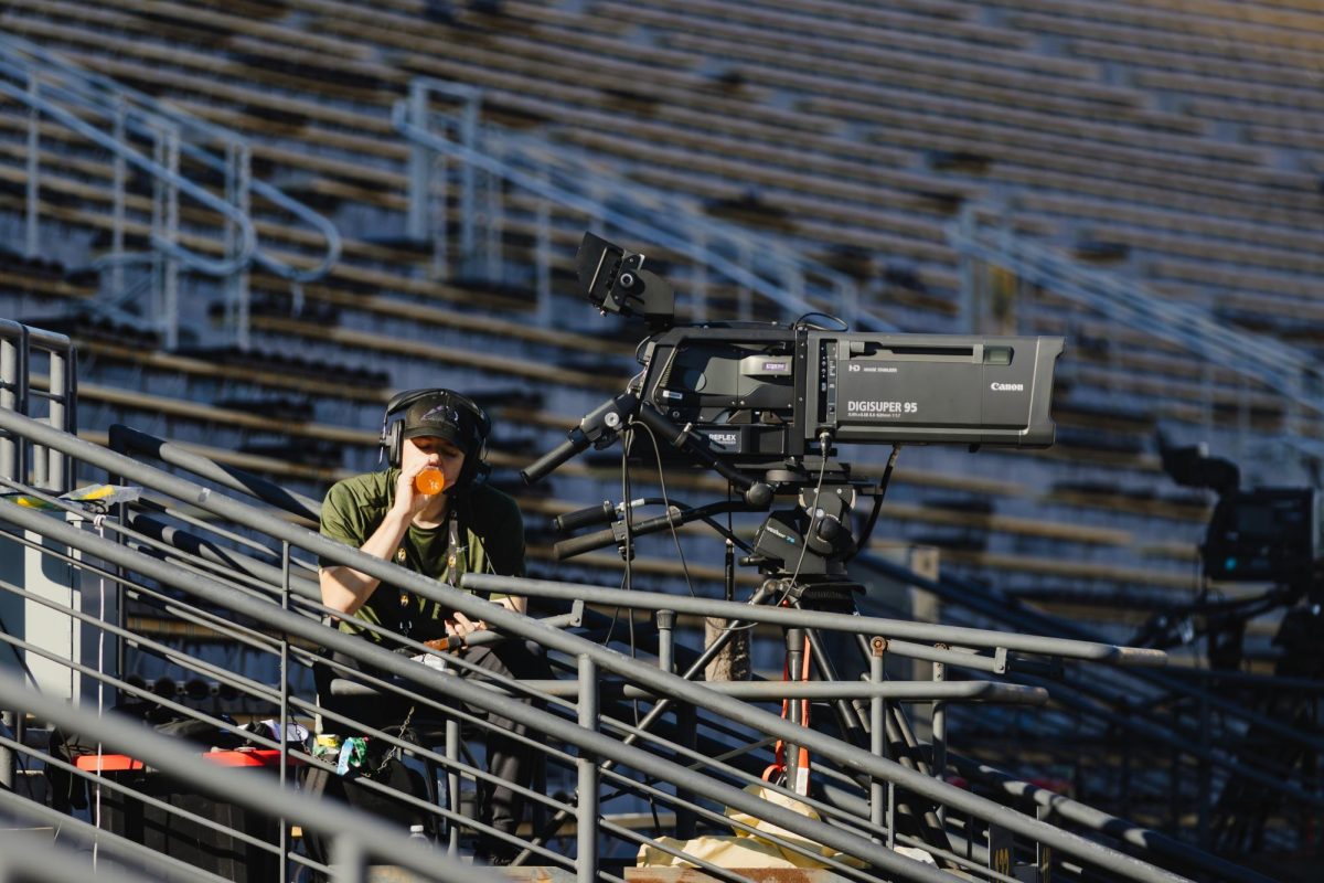 A man drinks a beverage next to a video camera